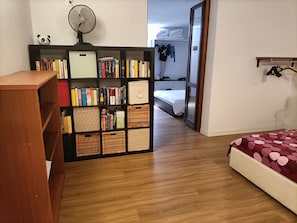 A room with a wooden bookshelf, a bed with a polka dot bedspread, and a wardrobe with hanging clothes. - S'Ulivariu (Donigala Fenughedu)