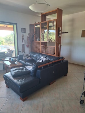 A living room with a black leather sofa, a wooden coffee table, and a large window offering a view of the outdoors. - S'Ulivariu (Donigala Fenughedu)