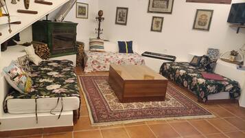 Una sala de estar acogedora con sofá, una mesita de centro de madera, una cama con ropa de cama floral, una pequeña mesa con un teclado y una chimenea verde.