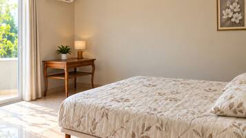 Ein Schlafzimmer mit einem Bett, einem Nachttisch mit Lampe, einer Zimmerpflanze und einem Fenster mit Vorhängen.