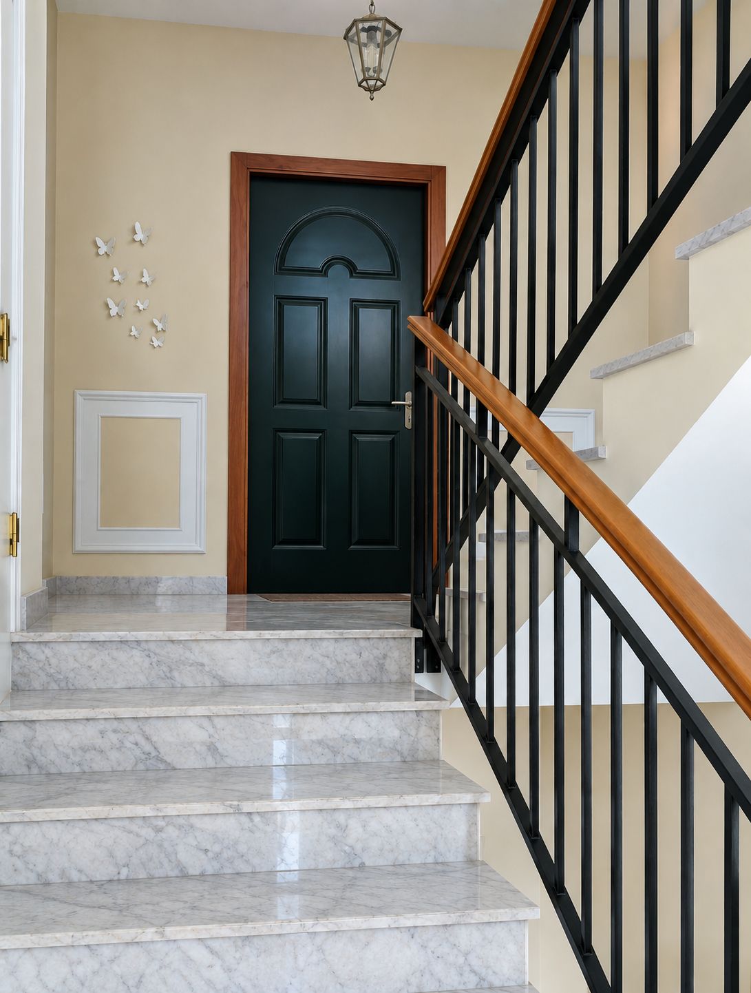 Una scalinata con gradini in marmo che conduce a una porta in legno scuro, con ringhiera in metallo nero e un lampadario a parete.