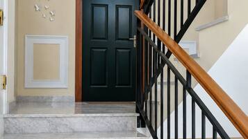 Una scalinata con gradini in marmo che conduce a una porta in legno scuro, con ringhiera in metallo nero e un lampadario a parete.