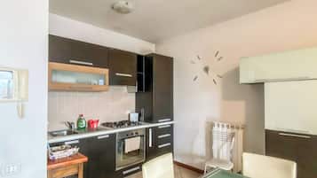 A modern kitchen with a dining area, including a table with chairs, a clock on the wall, and a built-in oven.