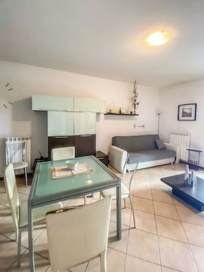 Een moderne woonkamer met een glazen eettafel, een bank en een keuken met kasten.