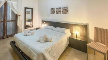 A hotel room with a bed, a chair, a nightstand with a lamp, a mirror, and artwork on the wall.