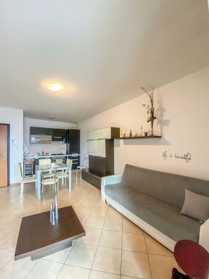 Een moderne woonkamer met een grijze bank, een bijzettafeltje en een eethoek met stoelen en een tafel.