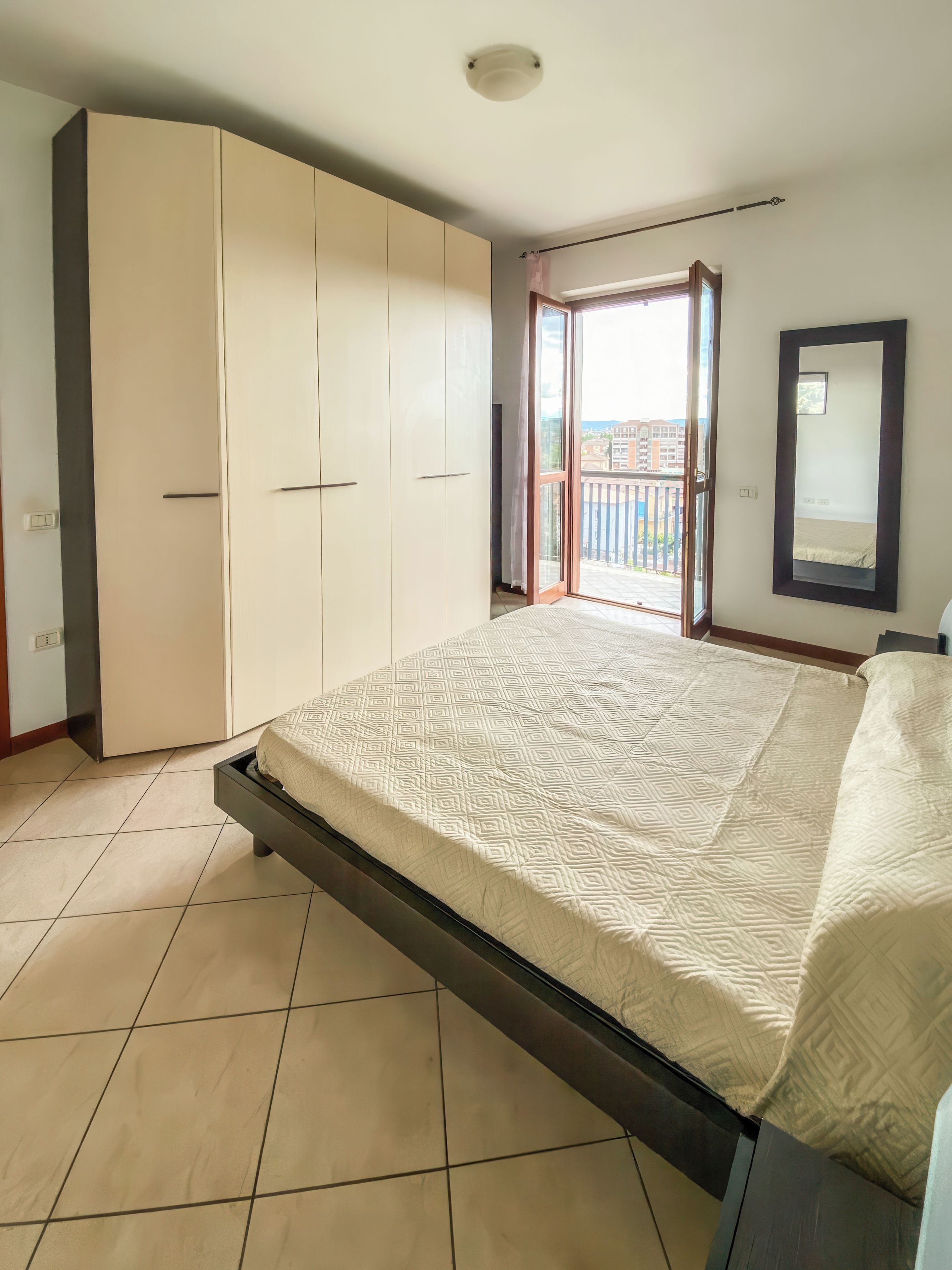 A bedroom with a bed, wardrobe, and a balcony.