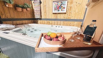 A hot tub with a wooden bench, a bowl of fruit, a glass of wine, and a bottle of liquor.