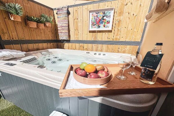 A hot tub with a wooden bench, a bowl of fruit, a glass of wine, and a bottle of liquor.