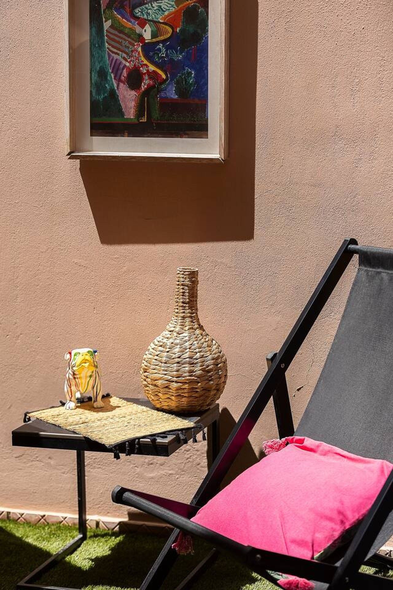A lounge chair with a pink cushion, a woven vase, and a small table with a decorative item.