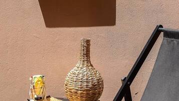 A lounge chair with a pink cushion, a woven vase, and a small table with a decorative item.