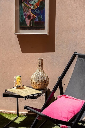 Een lounge stoel met een roze kussen, een gevlochten vaas en een bijzettafeltje met een decoratief object.