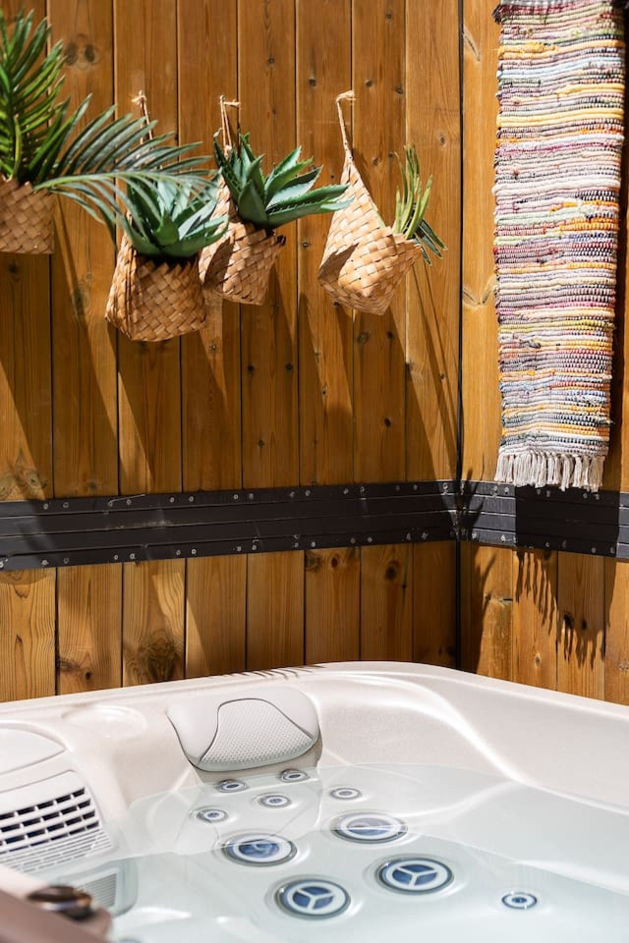 Un bain à remous doté d’un panneau de commande, un panier en osier contenant des plantes et une clôture en bois.
