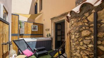 Un espace spa comprenant un jacuzzi, deux chaises longues, un mur en bois orné d’un tableau et un mur en pierre.
