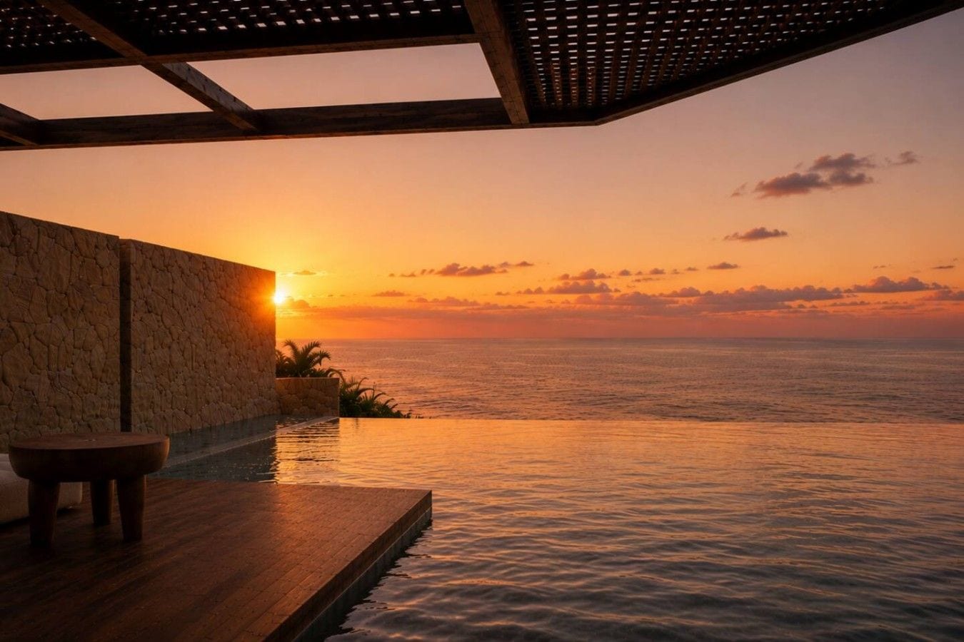 A sunset view from an infinity pool with a stone wall and a wooden deck.