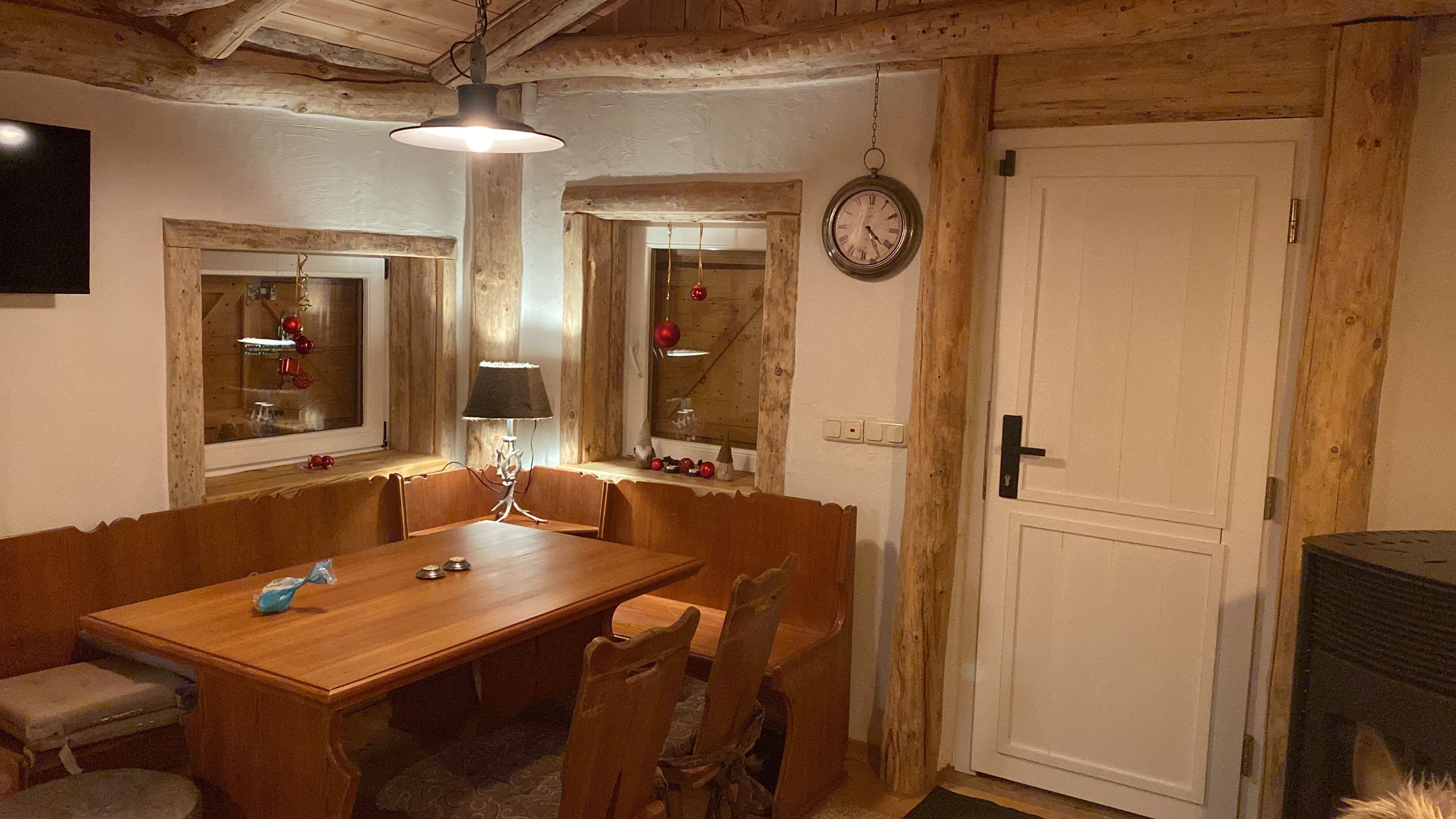 A dining room with a wooden table and chairs, a lamp, and a wall clock.