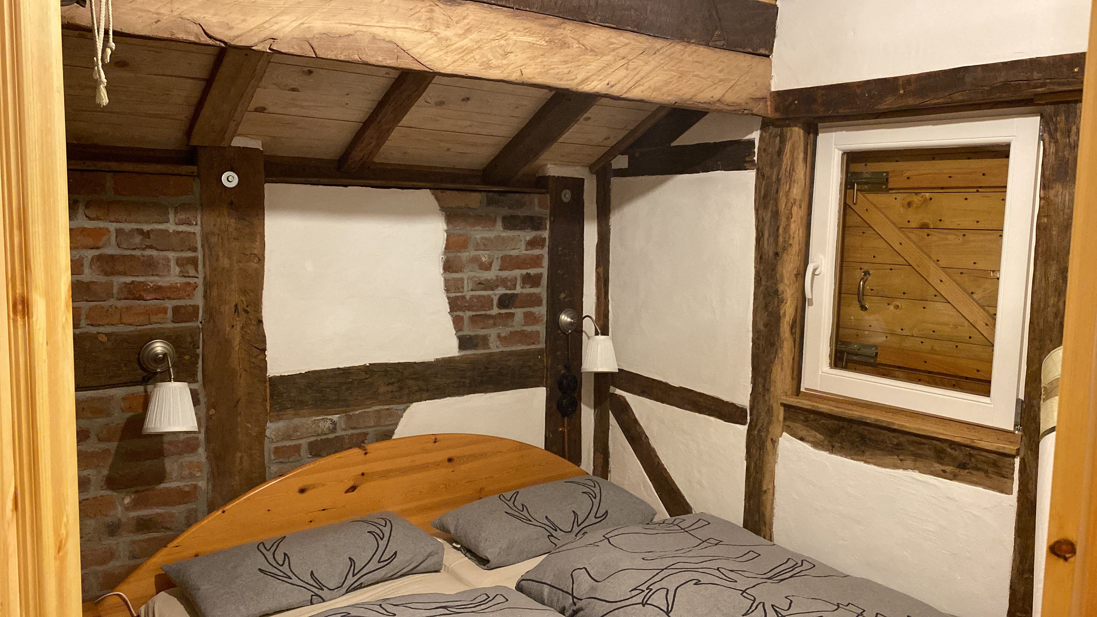 Ein rustikaler Raum mit freiliegenden Holzbalken, einer Ziegelwand und einem Bett mit gemusterten Kissen.