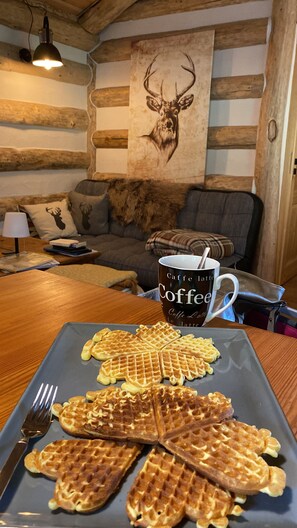 A cozy room with a wooden ceiling, a wall-mounted deer head artwork, a coffee mug on a table, and a plate of waffles. - Escape the daily grind and immerse yourself in nature! Enjoy this cozy forest cabin! (Bad Berleburg)