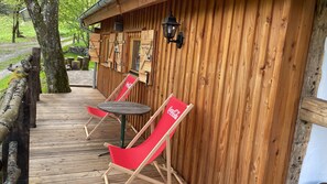 Eine Holzterrasse mit zwei roten Liegestühlen und einem Tisch, ein hölzernes Gebäude mit Satteldach und ein Holzzaun.