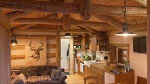 Interior rústico de una cabaña con techo de madera, un cuadro de un ciervo, una kitchenette y una zona de estar acogedora.