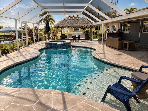 A swimming pool with a hot tub, surrounded by patio furniture and a covered area.