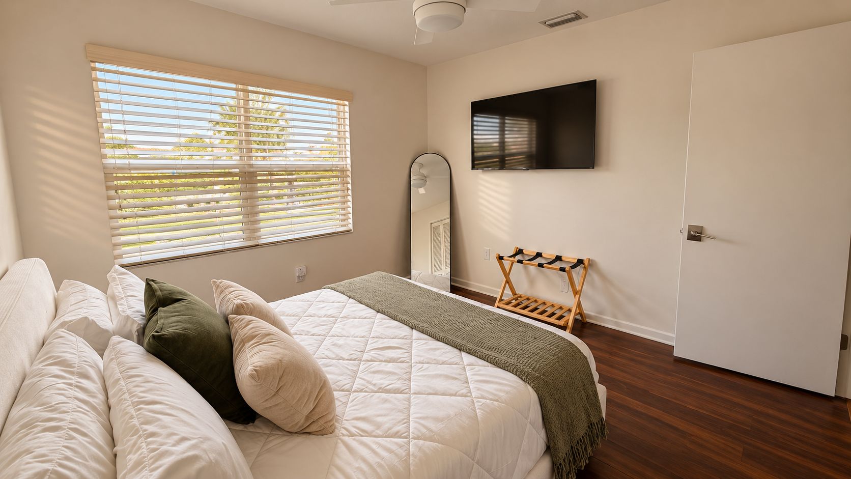 Une chambre à coucher avec un lit, un téléviseur fixé au mur, une fenêtre avec des stores et une porte.