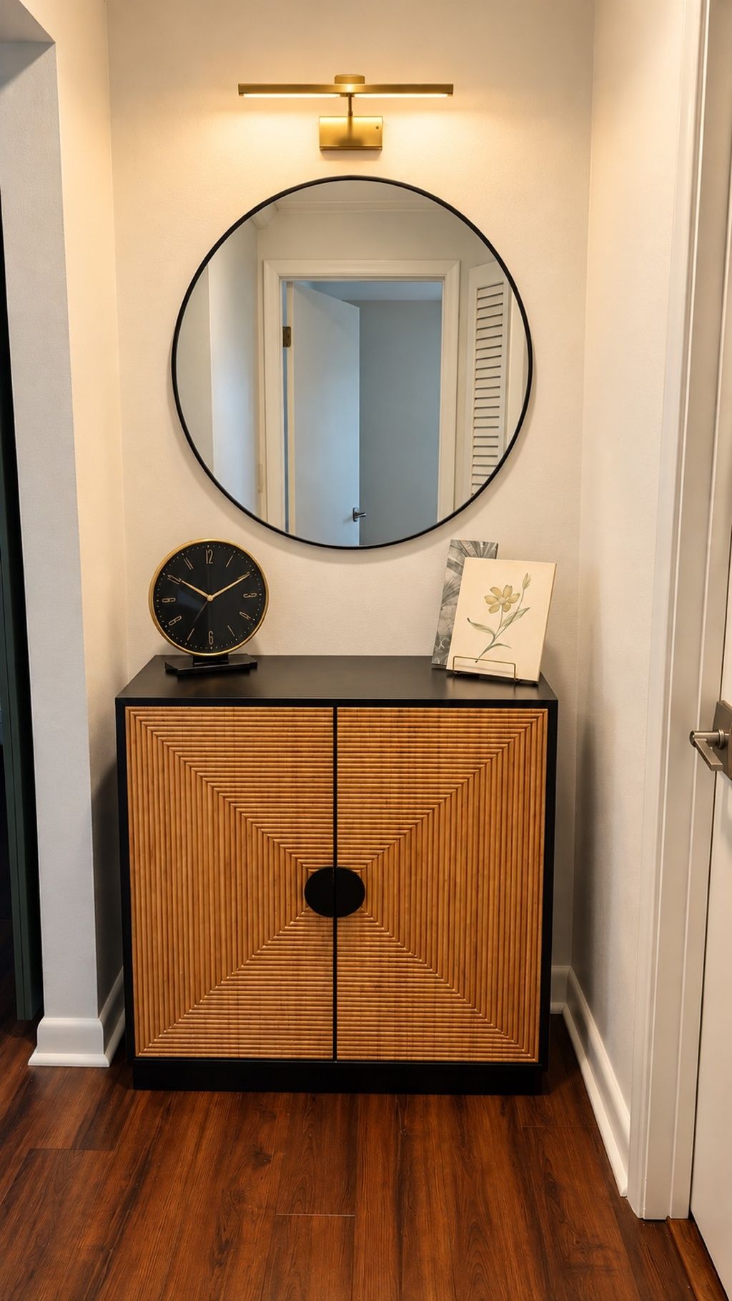 A wooden cabinet with a round mirror above it, a clock, and a framed picture on the top.