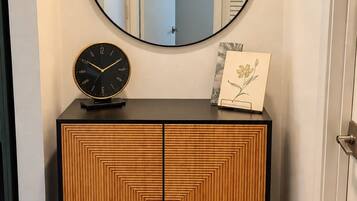 A wooden cabinet with a round mirror above it, a clock, and a framed picture on the top.