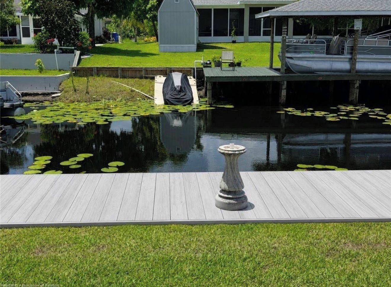 Un muelle de madera que lleva a un estanque tranquilo con lirios acuáticos, un pedestal de piedra y un bote cubierto.
