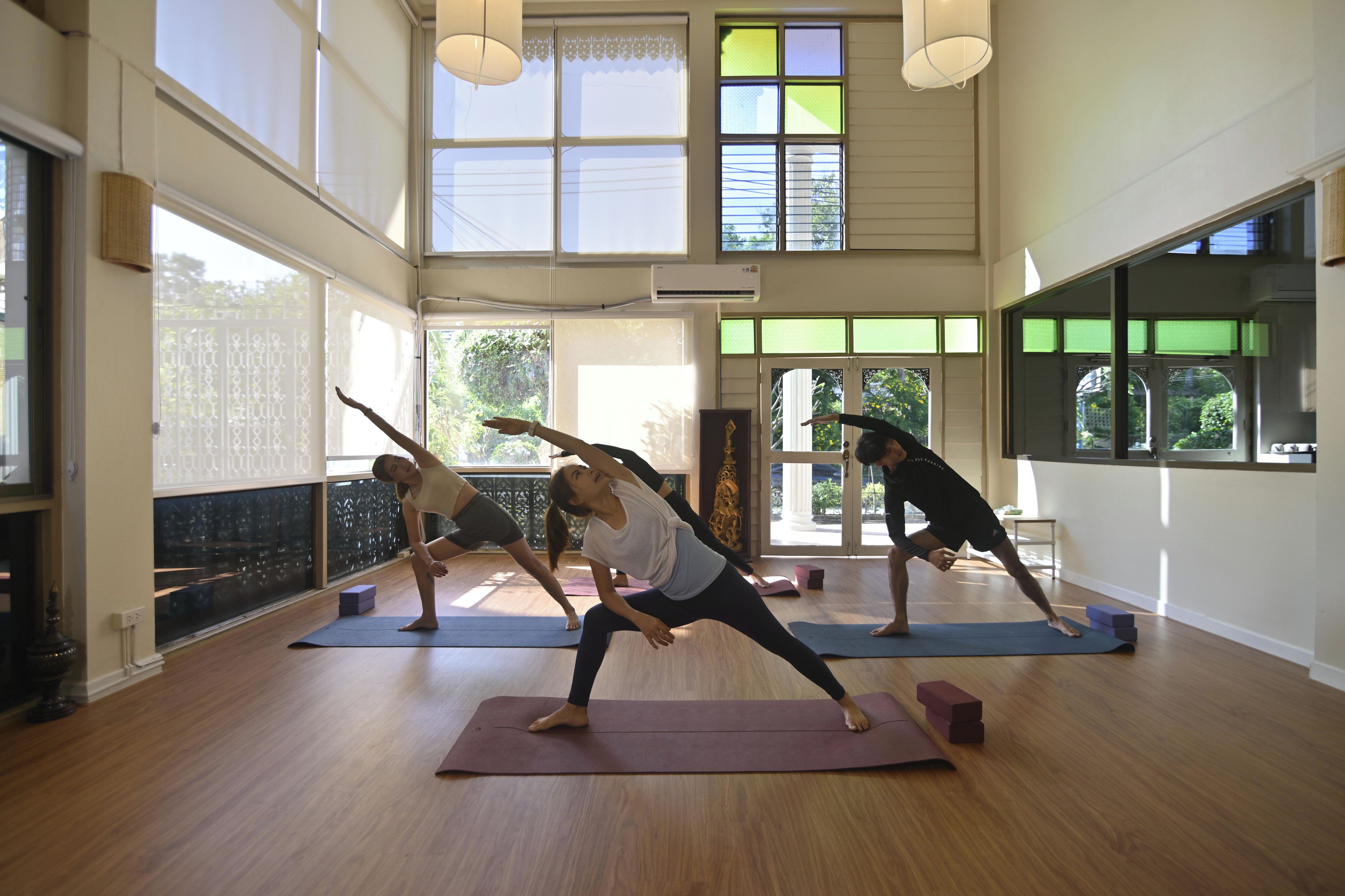 A spacious room with large windows, wooden floors, and a yoga mat area.