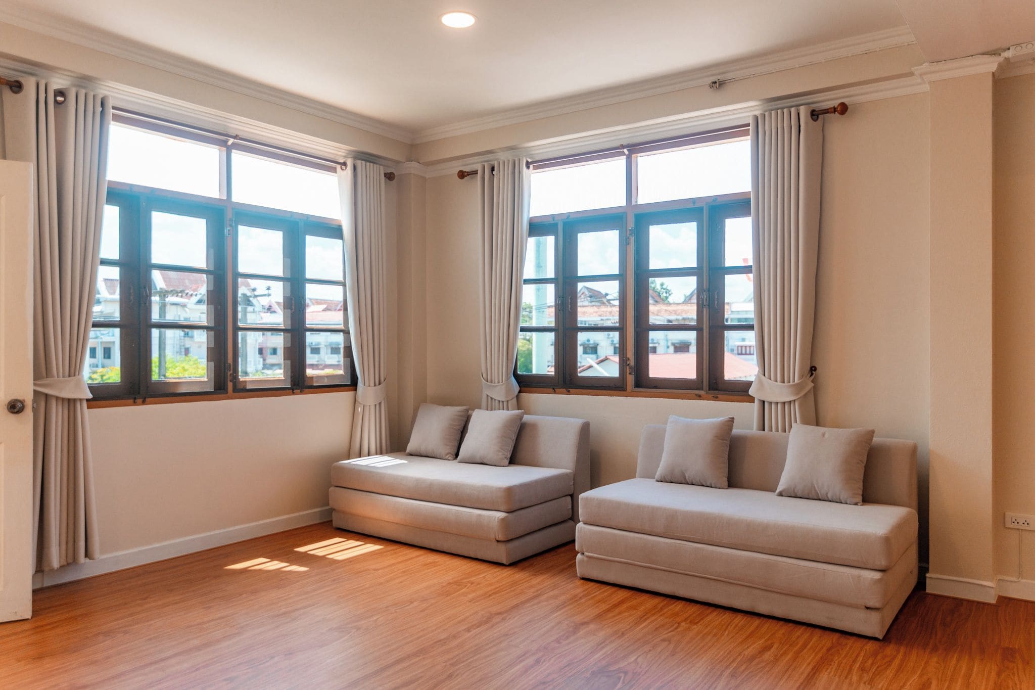 Una habitación con dos sofás, ventanas amplias, suelo de madera y techo blanco.