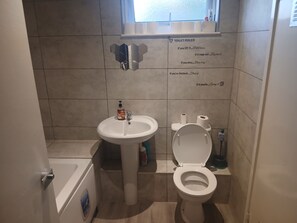 Un baño pequeño con inodoro, lavamanos y una ventana sobre el inodoro.