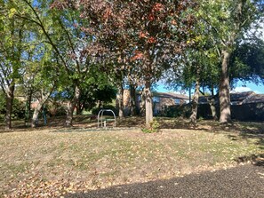 A park with trees, a playground, and a building in the background. - Mk apartment.  (Hodge Lea)
