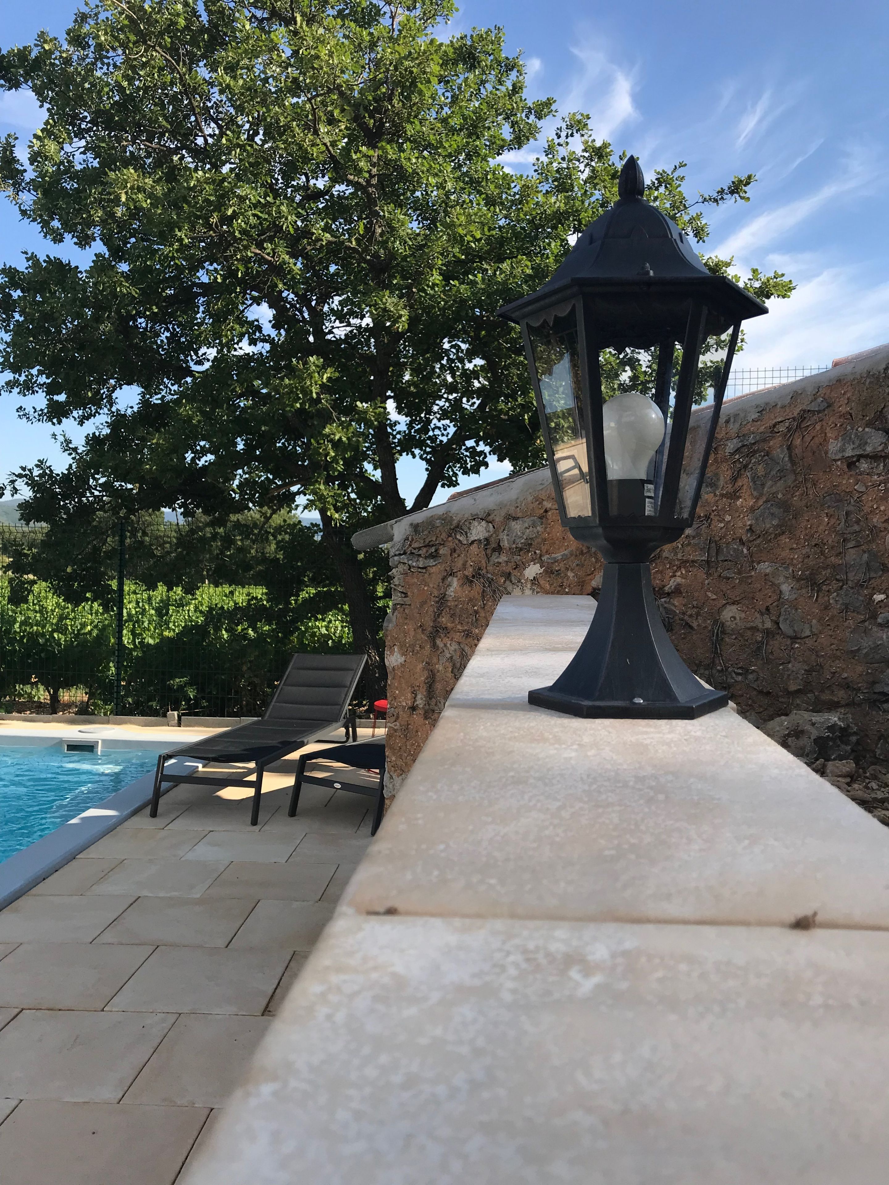 A poolside area with a stone wall, a lamp post, and lounge chairs.