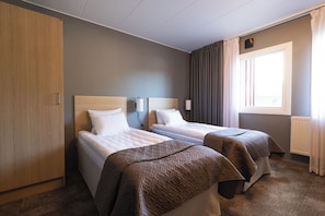 Habitación de hotel con dos camas, un armario, una ventana con cortinas y una lámpara fijada a la pared.