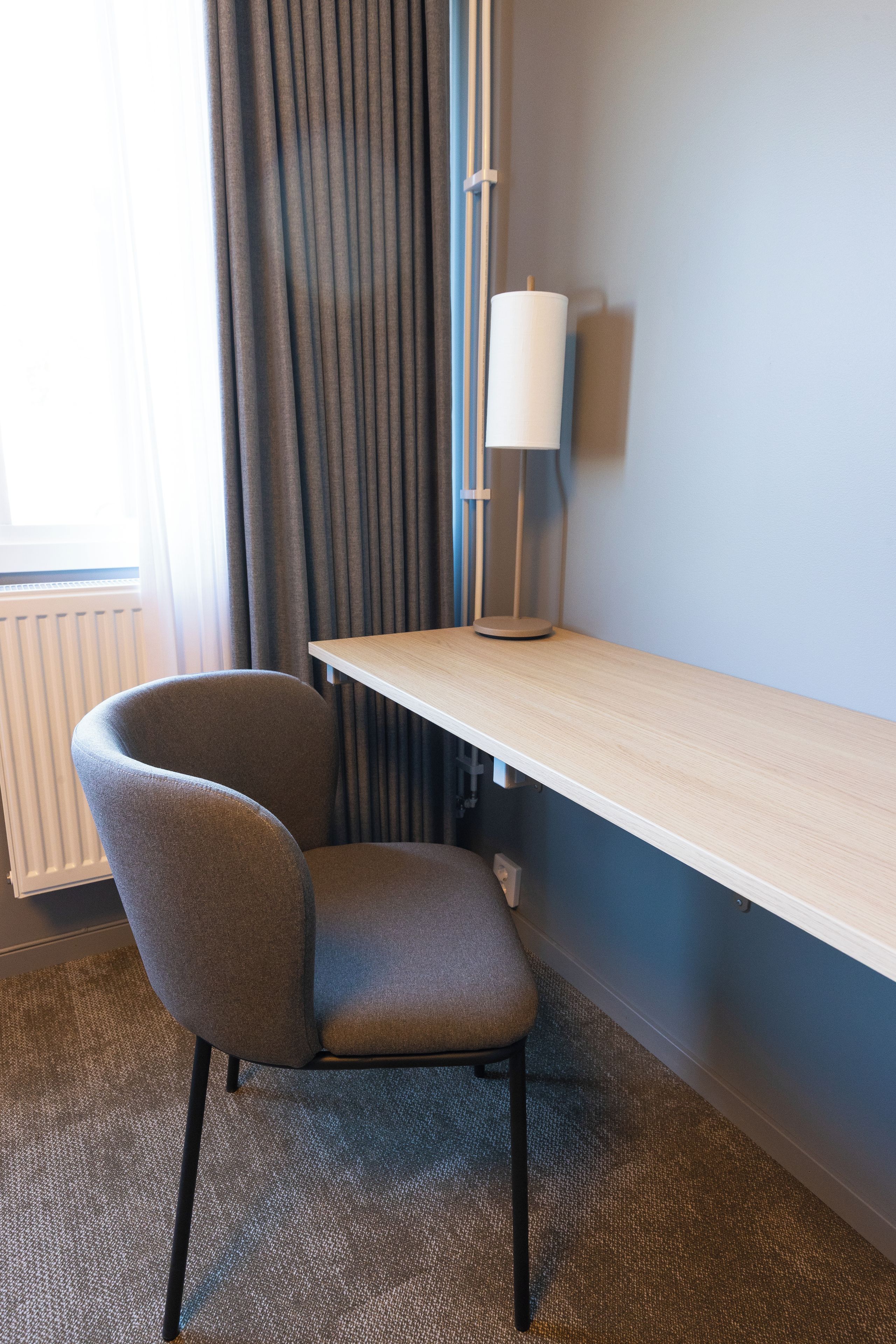 Ein Hotelzimmer mit Schreibtisch, Stuhl, Lampe und Blick ins Freie.