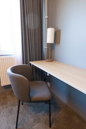 Una habitación de hotel con escritorio, silla, lámpara y vistas al exterior.