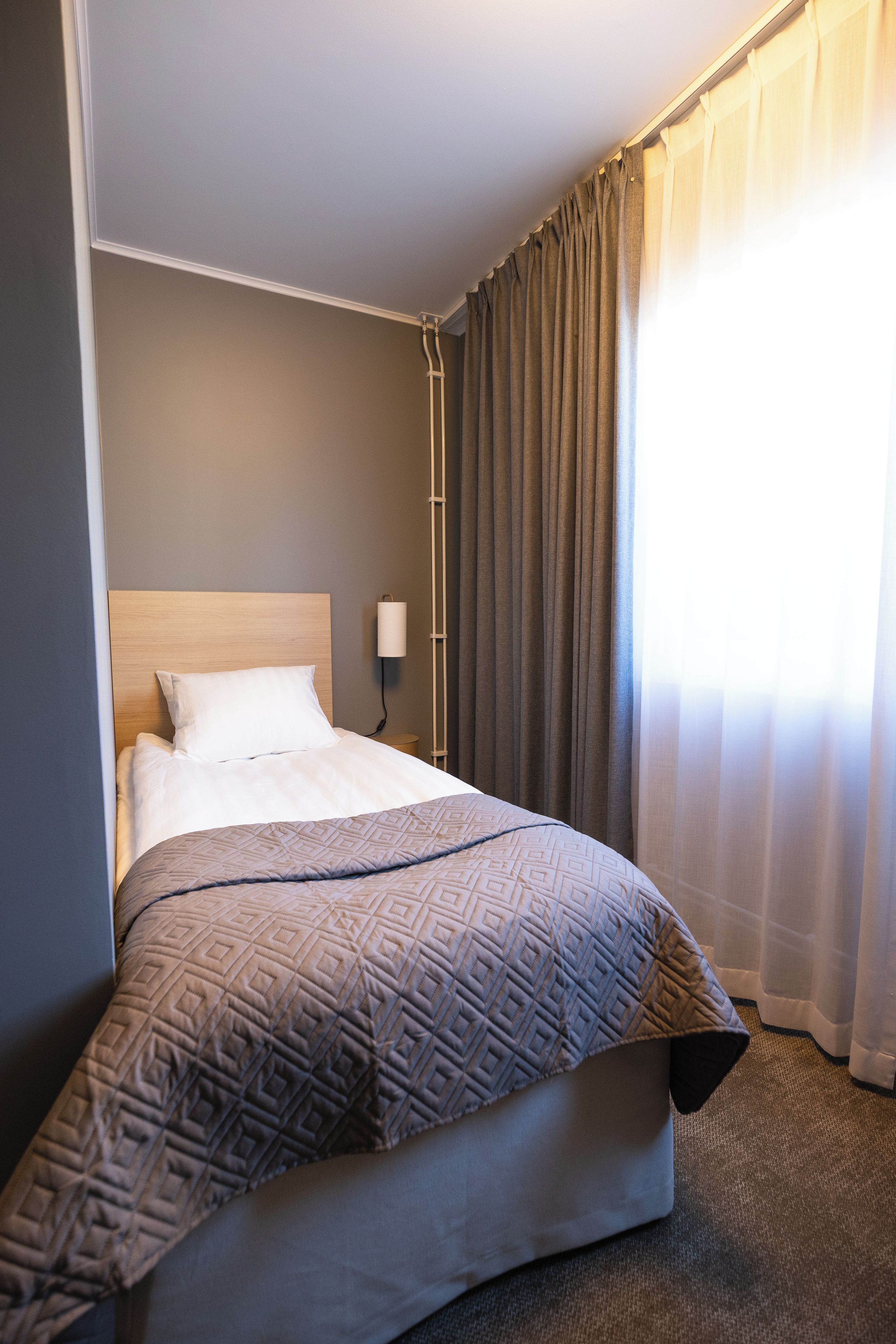 Ein Hotelzimmer mit einem Bett, einer Nachttischlampe und einem Fenster mit Vorhängen.