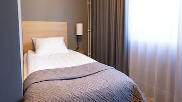 Ein Hotelzimmer mit einem Bett, einer Nachttischlampe und einem Fenster mit Vorhängen.