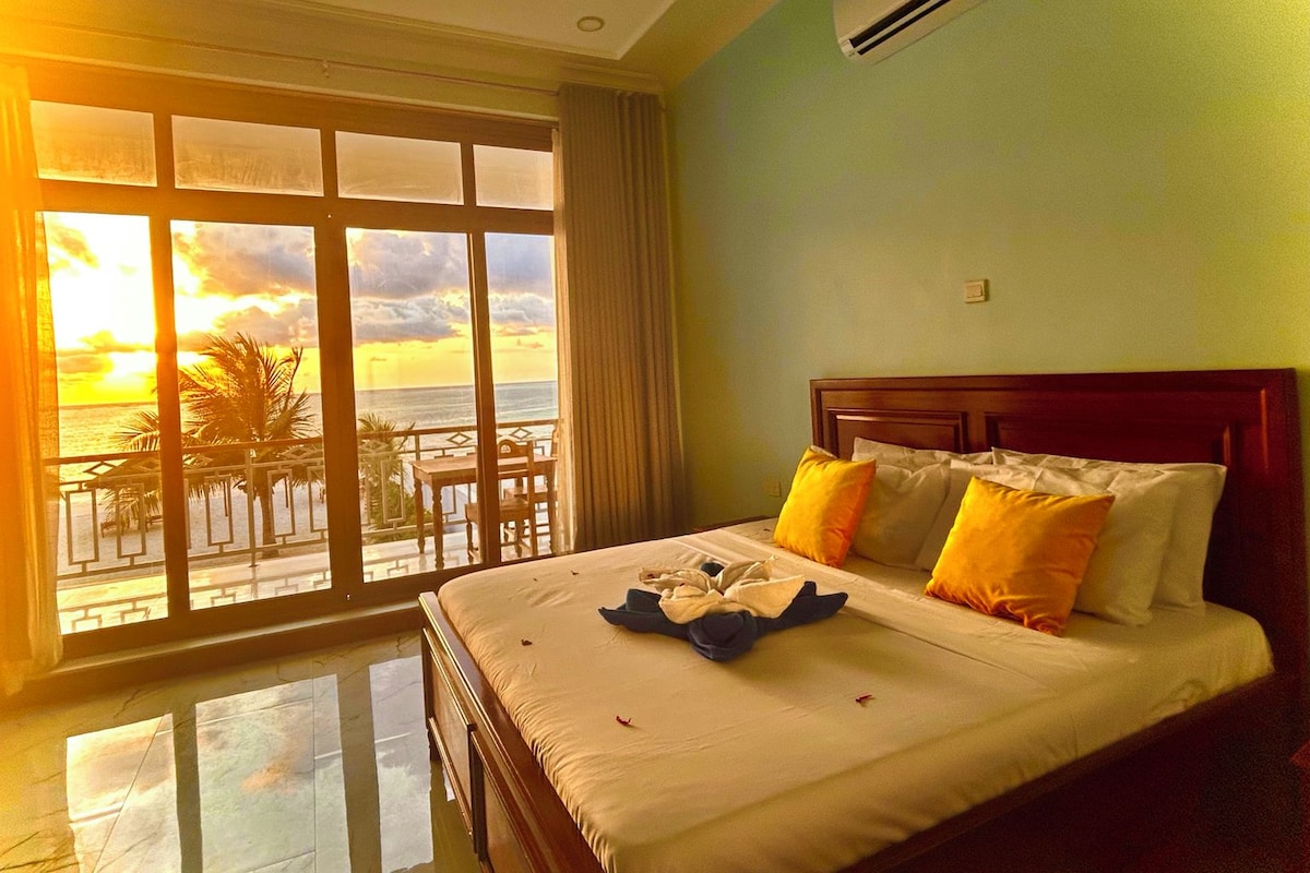 Une chambre d’hôtel dotée d’une grande fenêtre donnant sur l’océan et offrant une vue sur le coucher de soleil.
