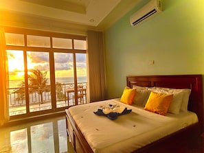 Une chambre d’hôtel dotée d’une grande fenêtre donnant sur l’océan et offrant une vue sur le coucher de soleil.
