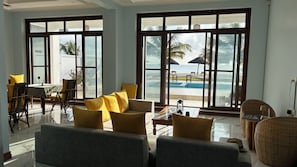 Une chambre avec vue sur la piscine, un coin repas et des sièges agrémentés de coussins jaunes.