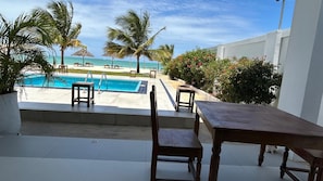 Une piscine avec vue sur l’océan, entourée de palmiers et bordée d’un bâtiment blanc.