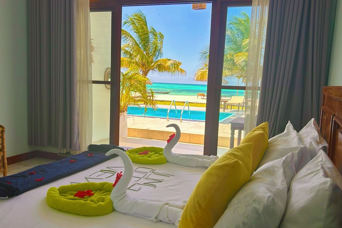 Une chambre d’hôtel avec un lit, un oreiller en forme de cygne et une vue sur une plage et l’océan.