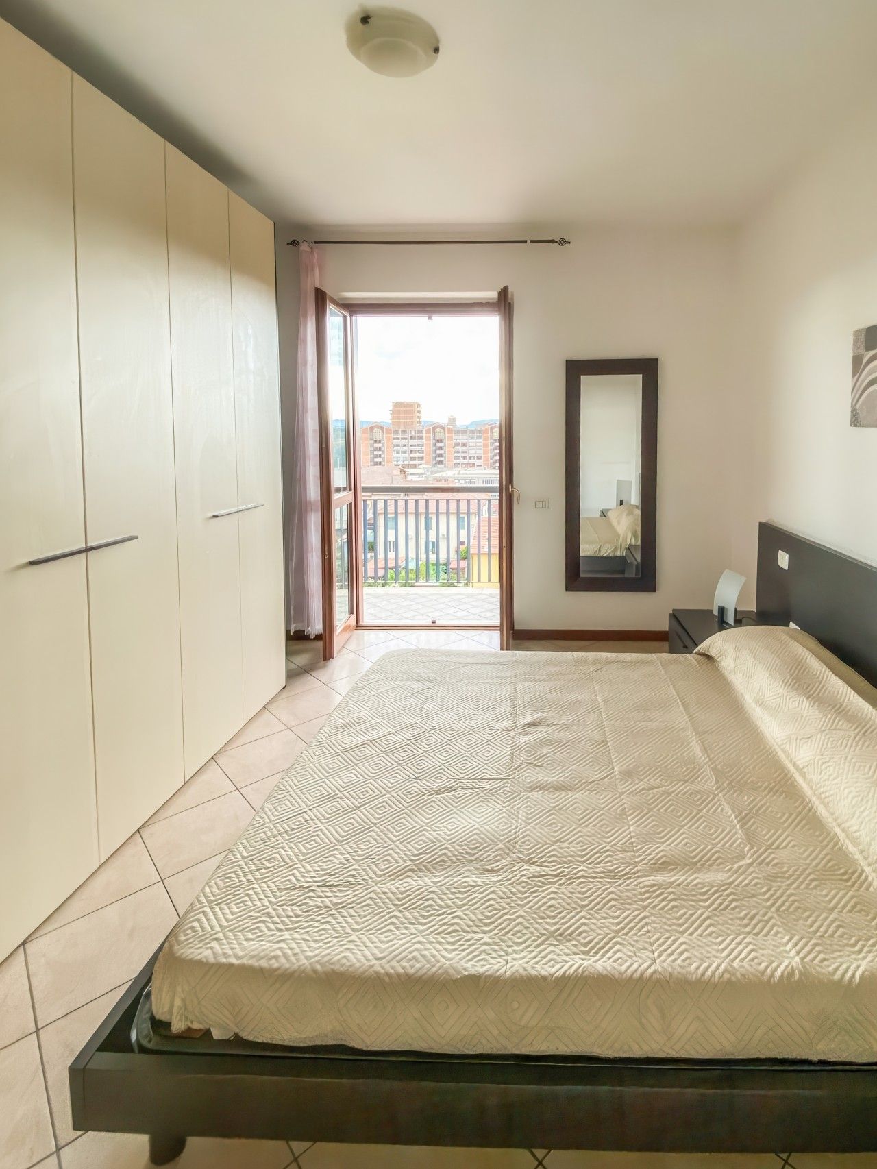 Ein Schlafzimmer mit Bett, Kleiderschrank und Blick auf einen Balkon.