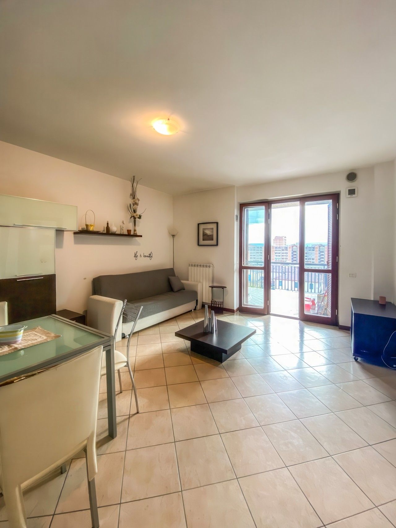 Un salón moderno con un sofá, una mesa de vidrio y vistas a un balcón exterior por medio de una puerta corrediza de cristal.