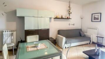 Un salon moderne avec une table à manger en verre, un canapé et un coin cuisine doté de placards.