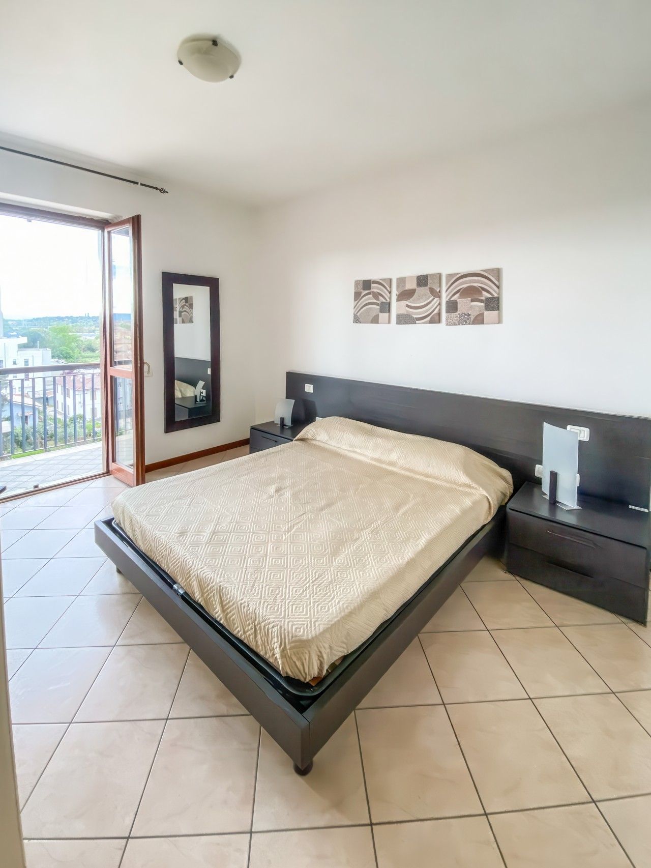 Une chambre à coucher avec un lit, une table de chevet, un miroir et des œuvres d’art accrochées au mur.