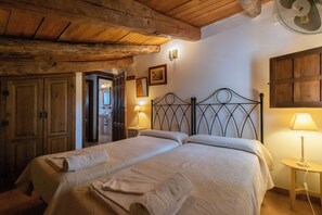 A room with a wooden ceiling, a bed with two pillows, a bedside table with a lamp, and a wardrobe.