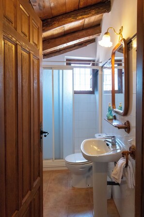 A bathroom with a wooden door, a white sink, a toilet, and a shower area.